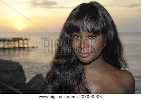 young attractive and glamorous African American black woman in chic and elegant summer dress posing relaxed on summer sunset beach in holiday vacation and beauty lifestyle concept
