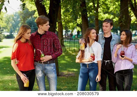 Jealousy and envy in friends relationship. Cheerful young people with detox cocktail having outdoor summer party