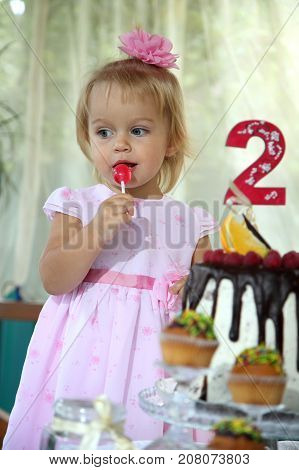Girl birthday. A little white-haired girl of two years is trying a birthday cake. Little girl celebrating second birthday.