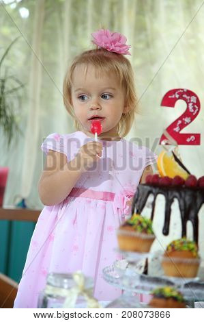 Girl birthday. A little white-haired girl of two years is trying a birthday cake. Little girl celebrating second birthday.