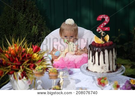 Girl birthday. A little white-haired girl of two years is trying a birthday cake. Little girl celebrating second birthday.