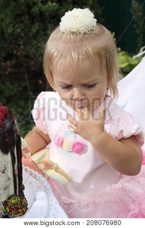Girl birthday. A little white-haired girl of two years is trying a birthday cake. Little girl celebrating second birthday.
