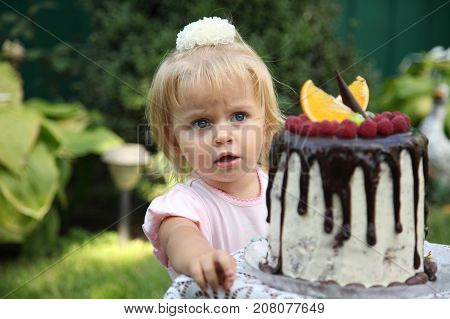 Girl birthday. A little white-haired girl of two years is trying a birthday cake. Little girl celebrating second birthday.