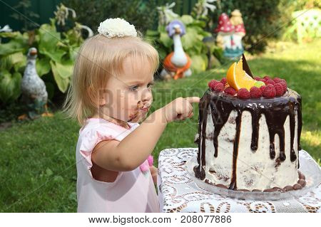 Girl birthday. A little white-haired girl of two years is trying a birthday cake. Little girl celebrating second birthday.