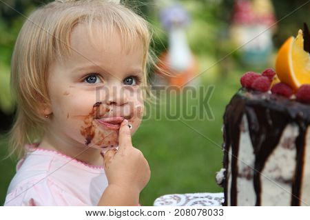 Girl birthday. A little white-haired girl of two years is trying a birthday cake. Little girl celebrating second birthday.