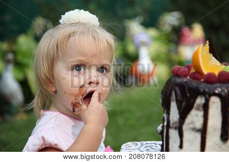 Girl birthday. A little white-haired girl of two years is trying a birthday cake. Little girl celebrating second birthday.