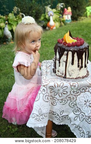 Girl birthday. A little white-haired girl of two years is trying a birthday cake. Little girl celebrating second birthday.