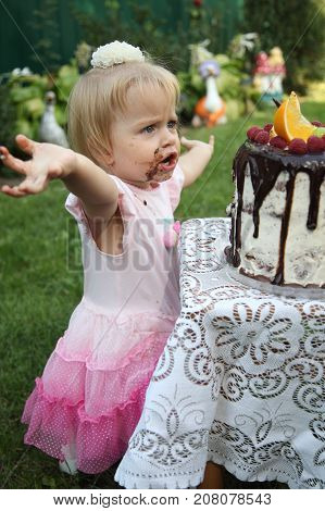 Girl birthday. A little white-haired girl of two years is trying a birthday cake. Little girl celebrating second birthday.