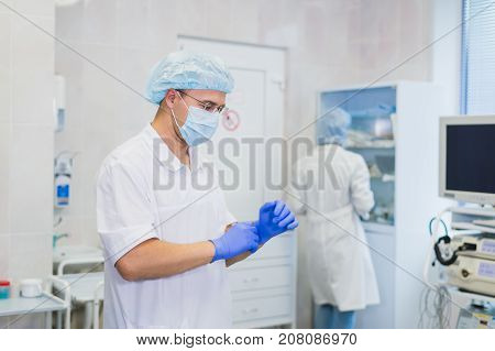 Young doctor during preparation for operation. Assistant of surgeon wearing surgical mask in operation room at the hospital