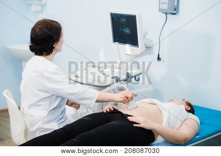 Pregnant woman looking at ultrasound shots of her growing baby showed by her doctor during medical examination.