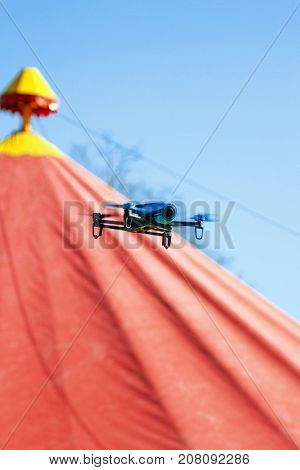 Blue drone flying over red circus tent against a blue sky in summer time and shoots a video