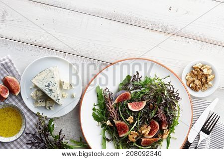 Salad with figs, blue cheese, arugula, mizuna and walnuts on white wooden background, top view