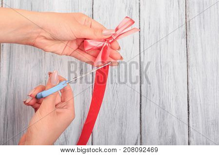 Hands with scissors, cut off a red ribbon. Close-up. On a gray background.