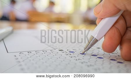 Students hand testing doing examination with pen drawing selected choice on answer sheets in school exams blur pupils college backgroud. Education system tests concept.