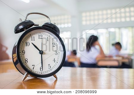 Closeup of Retro alarm clock with ten o'clock on table teacher in blur students exams classroom. Time is indefinite continued progress of existence. Education concept selective focus.