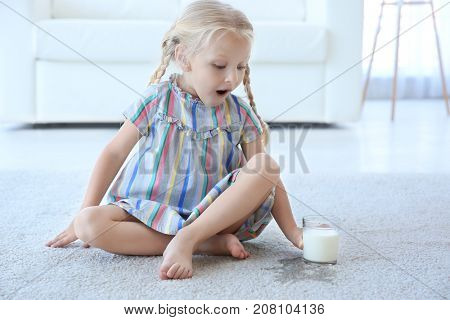 Cute little girl with glass of milk sitting on carpet near wet spot