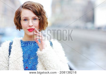 Portrait of young beautiful pensive woman in glasses on a city street in the blurry background. Close-up.