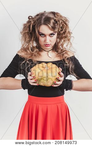 Portrait of woman holding in hands orange pumpkin isolated on gray background. Wearing black blouse and red skirt. Halloween celebration. Vertical shot