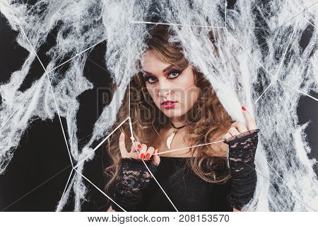 Portrait of Beauty Sexy Witch girl caught in a spider web. Fashion Art design. Beautiful Gothic model girl with Halloween make up and costume. Close-up shot