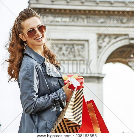 Stylish Christmas in Paris. Portrait of happy young woman  with shopping bags and Christmas present near Arc de Triomphe in Paris France