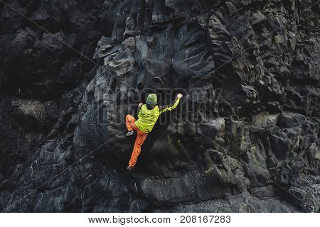 male rock climber. rock climber climbs on a black rocky wall on the ocean bank in Iceland, Kirkjufjara beach. man makes hard move without rope.