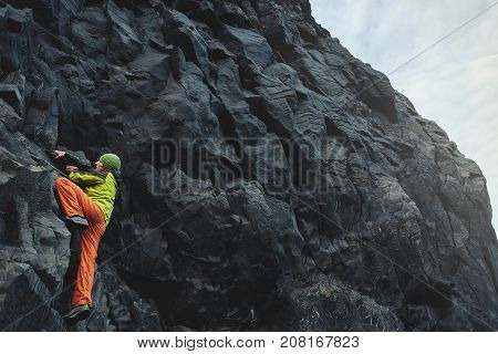 male rock climber. rock climber climbs on a black rocky wall on the ocean bank in Iceland, Kirkjufjara beach. man makes hard move without rope.