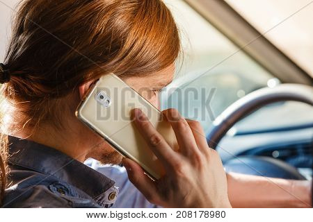 Talking while drive danger fresh driver concept. Young man driving car using his smartphone talking with someone.