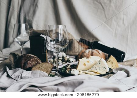 Two empty wineglasses are standing ready to be filled with dry red wine lying behind. Fresh bread, blue cheese, masdaam cheese and quail eggs are used as decoration. stylish shot