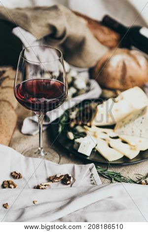 A wineglass is filled with dry red wine lying behind. Fresh bread, blue cheese, masdaam cheese, quail eggs and nuts are used as decoration. awesome