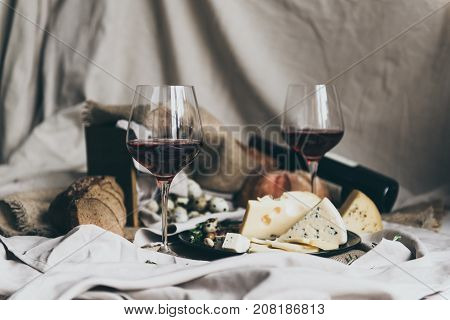 Two wineglasses are filled with dry red wine lying behind. Fresh bread, blue cheese, masdaam cheese and quail eggs are used as decoration. so delisious