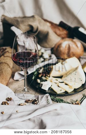 A wineglass is filled with dry red wine lying behind. Fresh bread, blue cheese, masdaam cheese, quail eggs and nuts are used as decoration. awesome