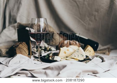 A wineglass is filled with dry red wine lying behind. Fresh bread, blue cheese, masdaam cheese, quail eggs and nuts are used as decoration. awesome