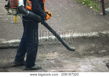 Worker On A Street In Autumn Collects Leaves With A Leaf Blower