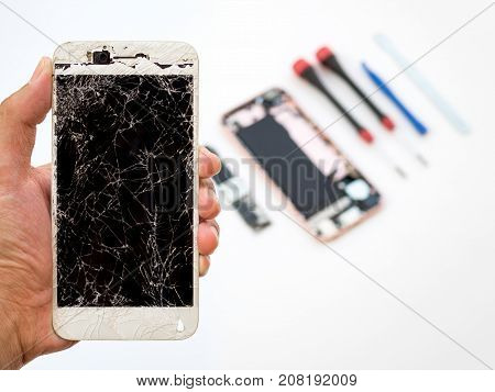 Close-up of cracked smartphone screen in technician hand on blurred smartphone component background with copy space