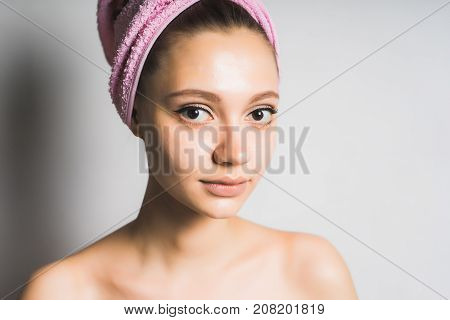 beautiful girl with a towel on her head is standing by the white wall