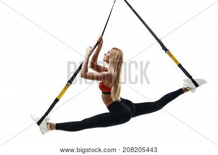 Beautiful young fitness woman in sportswear doing a split exercising with suspension straps isolated on white background