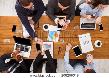 Business handshake. Agreement at meeting. Multiethnic team. Busy workers in office, top view of wooden table