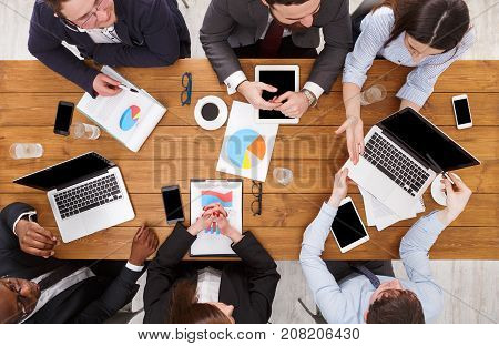 Multiethnic company meeting. Manager and emploees work in comfortable office, top view of wooden table