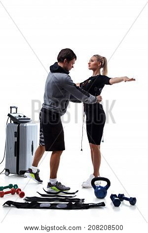 Trainer helps woman attaching electrode on ems suit isolated on white background