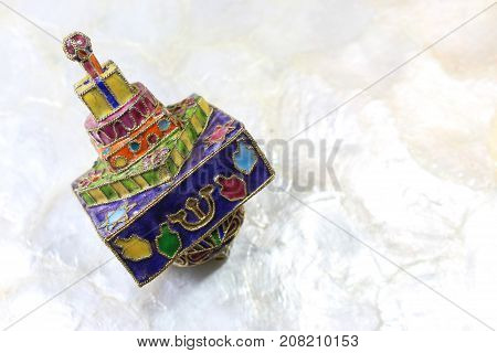 Brightly colored cloisonne Hanukkah dreidel on a soft white background