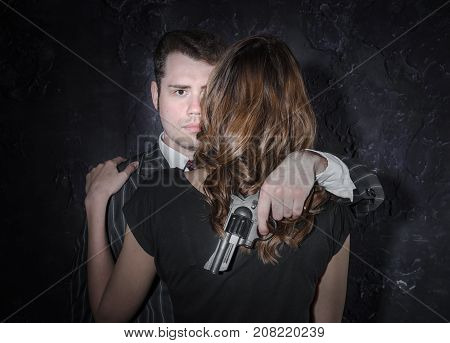 A Detective With A Gun And His Beautiful Woman In Retro Outfit Leaning On Him. Studio Shot. Noir Sty