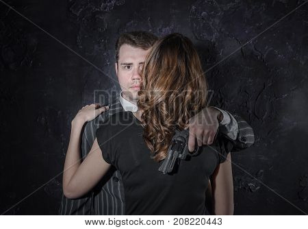 A Detective With A Gun And His Beautiful Woman In Retro Outfit Leaning On Him. Studio Shot. Noir Sty