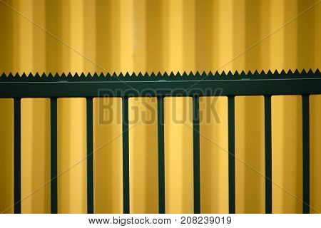 The side view yellow Cargo Containers in front of which is a striking pointed-jagged green fence.