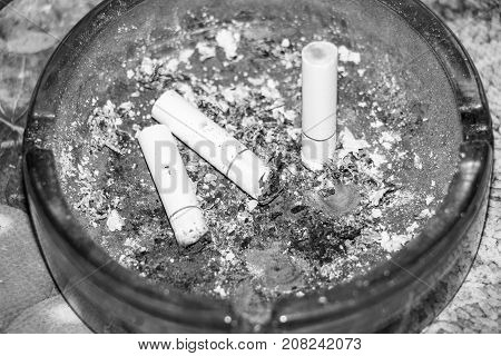 Three cigarette butts in the dark ashtray. Black and white photo