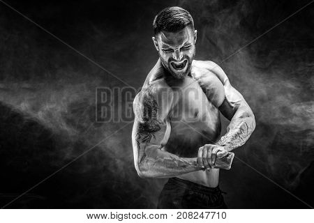Awesome power athletic man bodybuilder screaming while flexing his muscles. Fitness muscular body on dark smoke background. Perfect male.