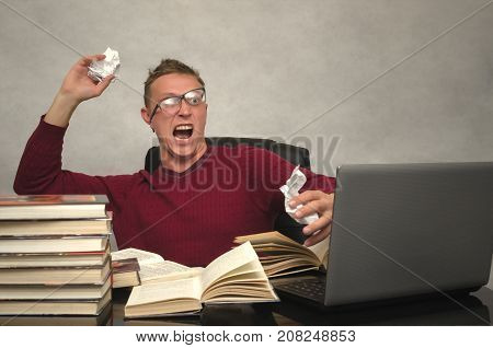 Young student man becomes hysterical from studying. Office worker goes crazy with overload at work. Mad student sitting at the table and throws the piece of paper and prevents to lead a lesson.
