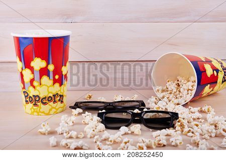 Bowl with scattered popcorn and 3D glasses on a wooden background
