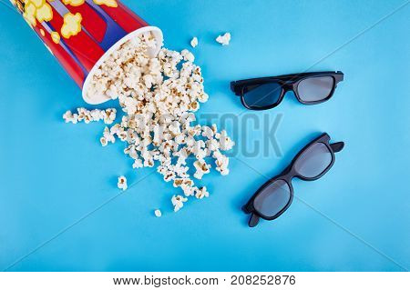 Spilled popcorn and two pairs of 3d glasses on a blue background. Close-up. View from above.
