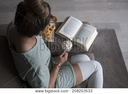 topview of woman reading book at home on couch with hot chocolatemilk and cookies