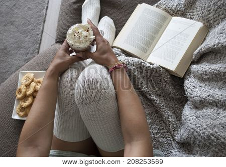 closeup of woman reading book at home on couch with hot chocolatemilk and cookies